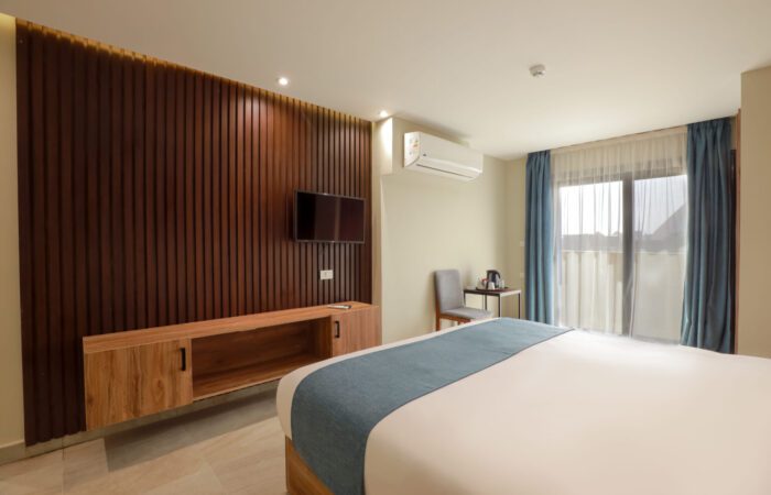 Modern bedroom with a bed, wall-mounted TV on a wood slat wall, air conditioner, and balcony with Pyramids View
