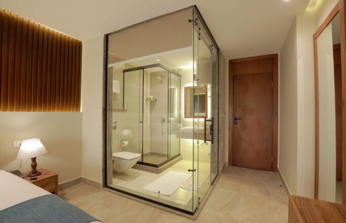 Modern hotel room featuring a central glass-enclosed bathroom with a shower, toilet, and sink