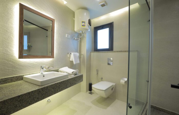 Modern bathroom with a backlit mirror, white sink on granite counter, wall-mounted toilet, and glass shower