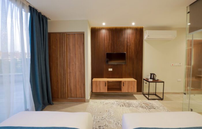 Modern hotel room with a wall-mounted TV, wooden wardrobe, floating console, and air conditioning