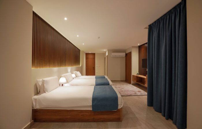 Triple hotel room with three single beds, white linens, blue throws, and modern wood paneling