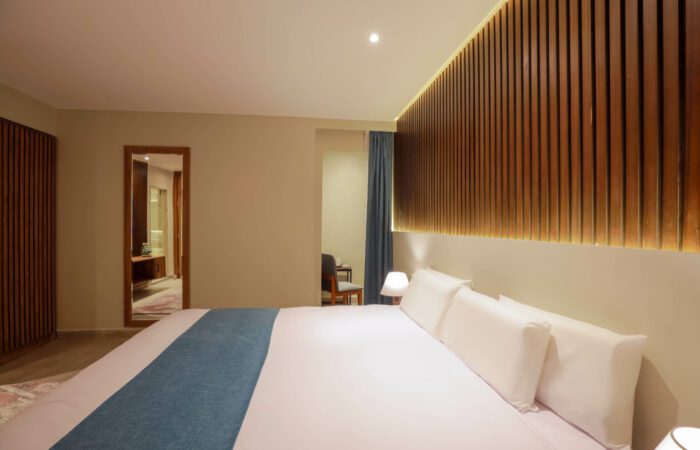 Modern hotel room with a large bed, white linens, blue runner, and a backlit wooden slat accent wall