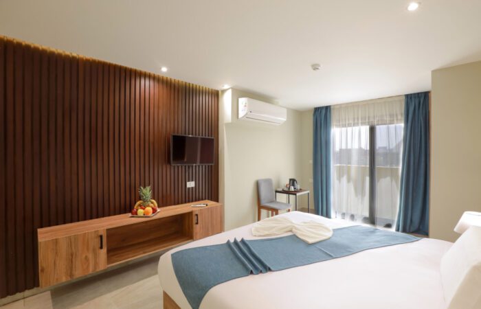 Modern hotel room with a bed, wood-slatted accent wall with a TV, and a window with blue curtains