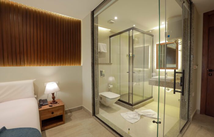 Modern hotel room with a bed and a glass-walled bathroom featuring a walk-in shower and vanity