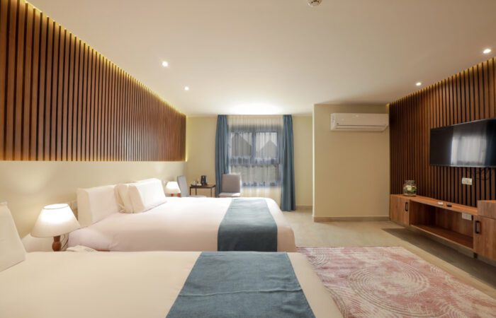 Modern hotel room with two large beds, wood-slat accent walls, a wall-mounted TV, and a balcony with Pyramids View