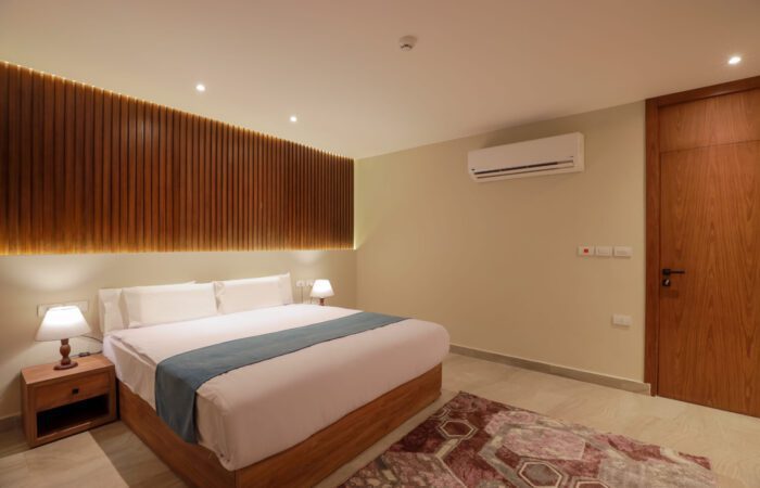 Modern hotel bedroom with a king-size bed, wooden slatted headboard, and warm ambient lighting
