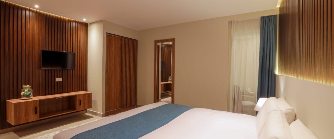 Modern bedroom with a large bed, wood-slat accent walls, a wall-mounted TV, and warm recessed lighting
