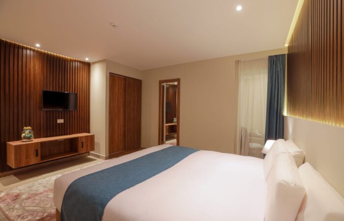 Modern bedroom with a large bed, wood-slat accent walls, a wall-mounted TV, and warm recessed lighting