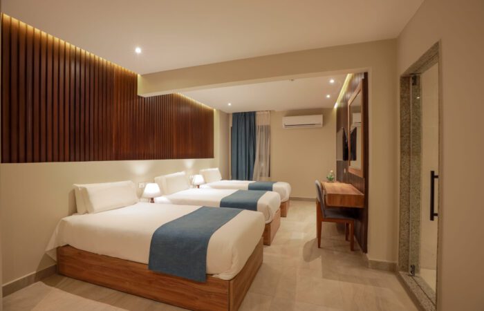 Modern hotel room with three single beds, blue bed runners, and a wooden slat accent wall