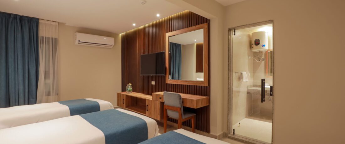 Triple hotel room with three single beds, a desk area with a TV, and an en-suite bathroom