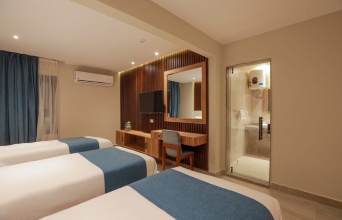 Triple hotel room with three single beds, a desk area with a TV, and an en-suite bathroom