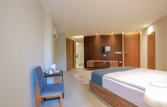 Modern hotel room with a bed, blue chair, and wall-mounted TV on a wood-paneled wall
