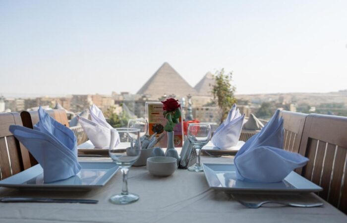 A set dinner table on a terrace overlooking the Great Pyramids of Giza