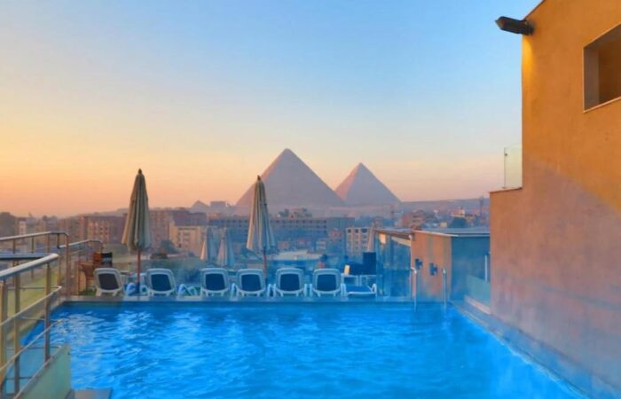 Rooftop swimming pool with lounge chairs overlooking the Great Pyramids of Giza at sunset