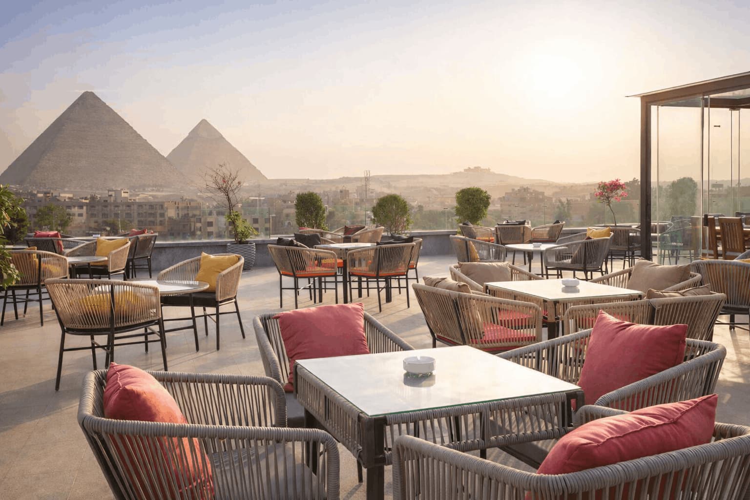 Rooftop restaurant with outdoor seating and a view of the Great Pyramids of Giza at sunset
