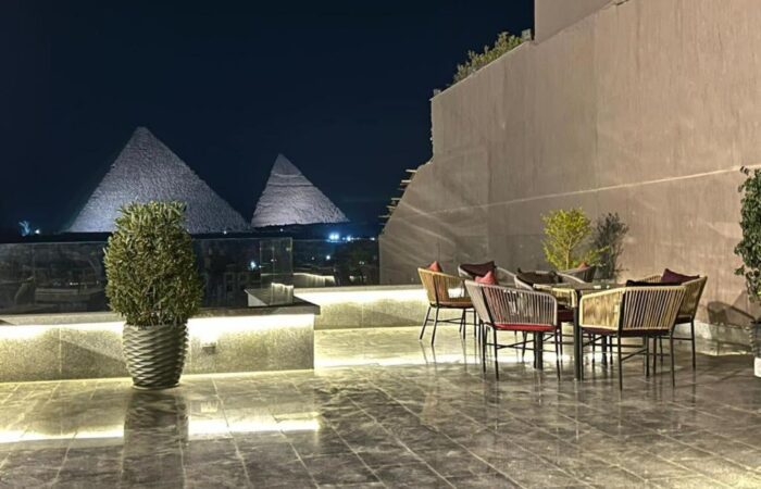 Nighttime view of the Great Pyramids of Giza from a modern rooftop terrace with outdoor seating